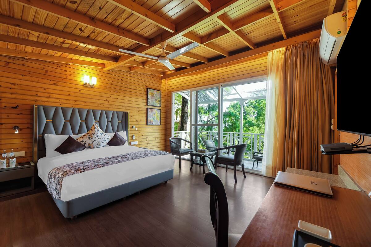 Um quarto com cama, mesas de cabeceira, escrivaninha, cadeira, laptop e janela com cortinas.