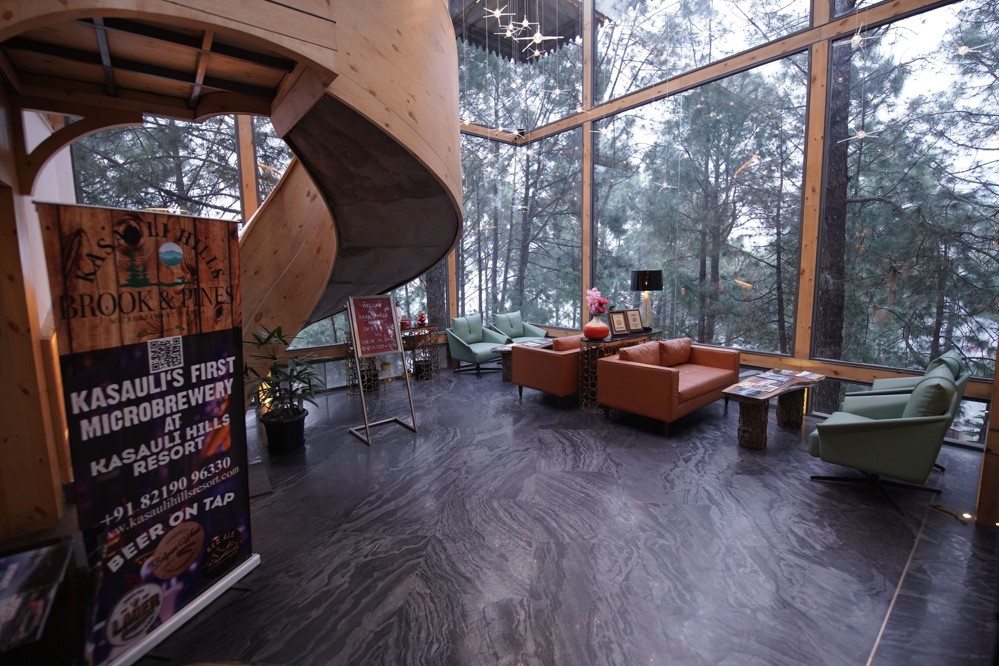 A modern interior with a wooden spiral staircase, large windows offering a forest view, and a seating area with sofas and a coffee table.