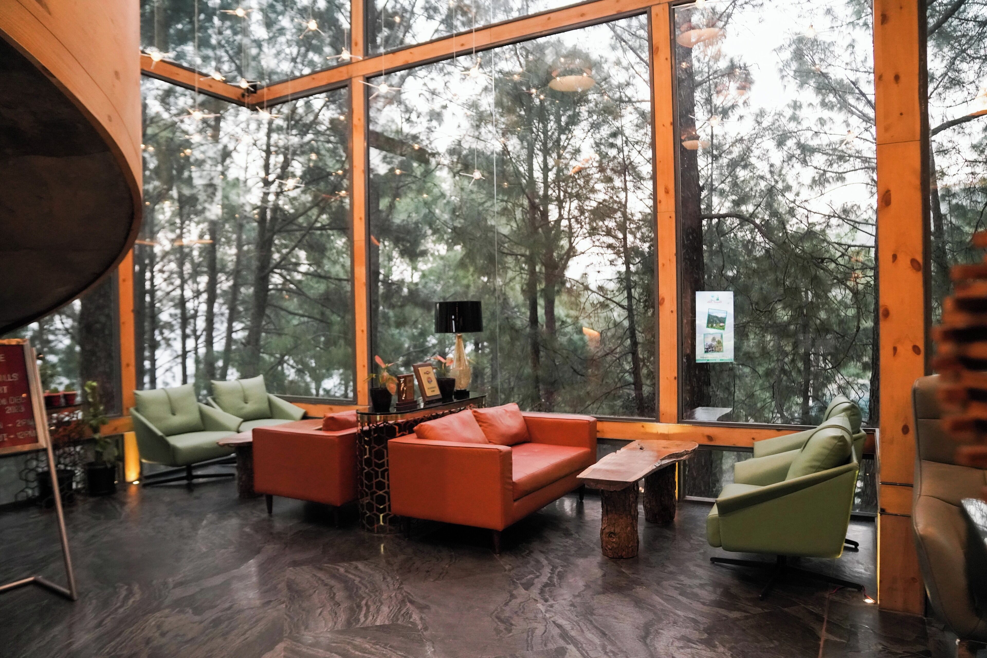 A modern interior with large windows, a green sofa, an orange sofa, and a wooden coffee table.