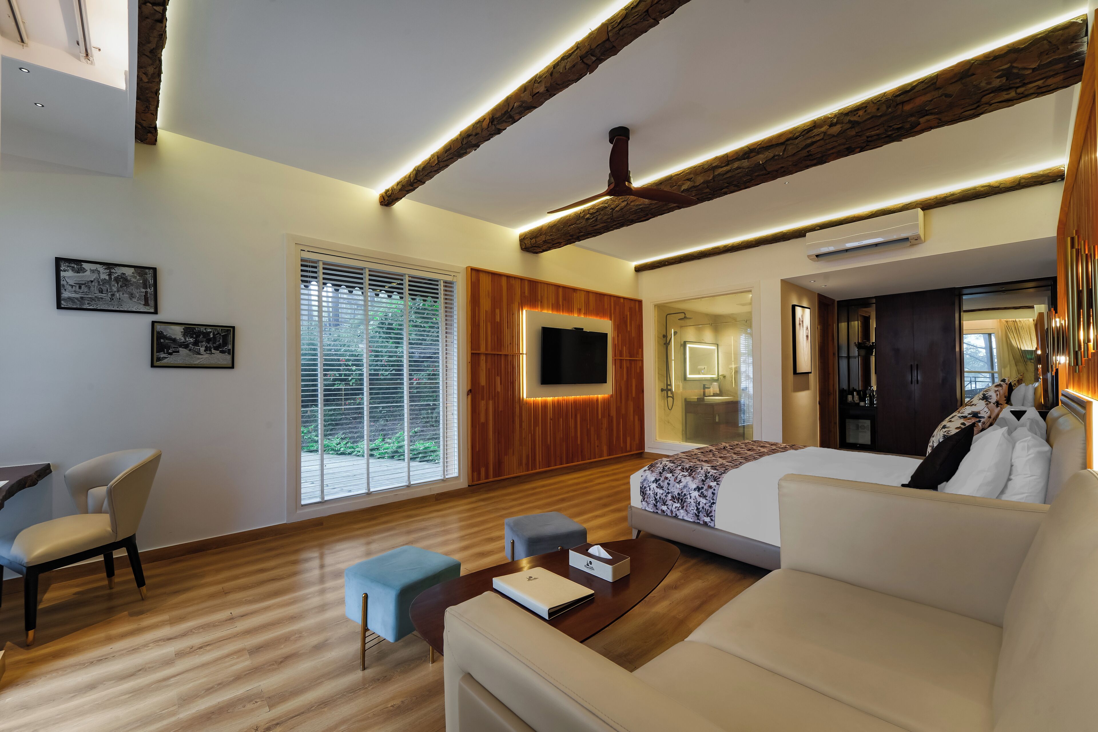 A modern hotel room with a wooden ceiling, a large bed, a sofa, a TV, and a desk with a chair.