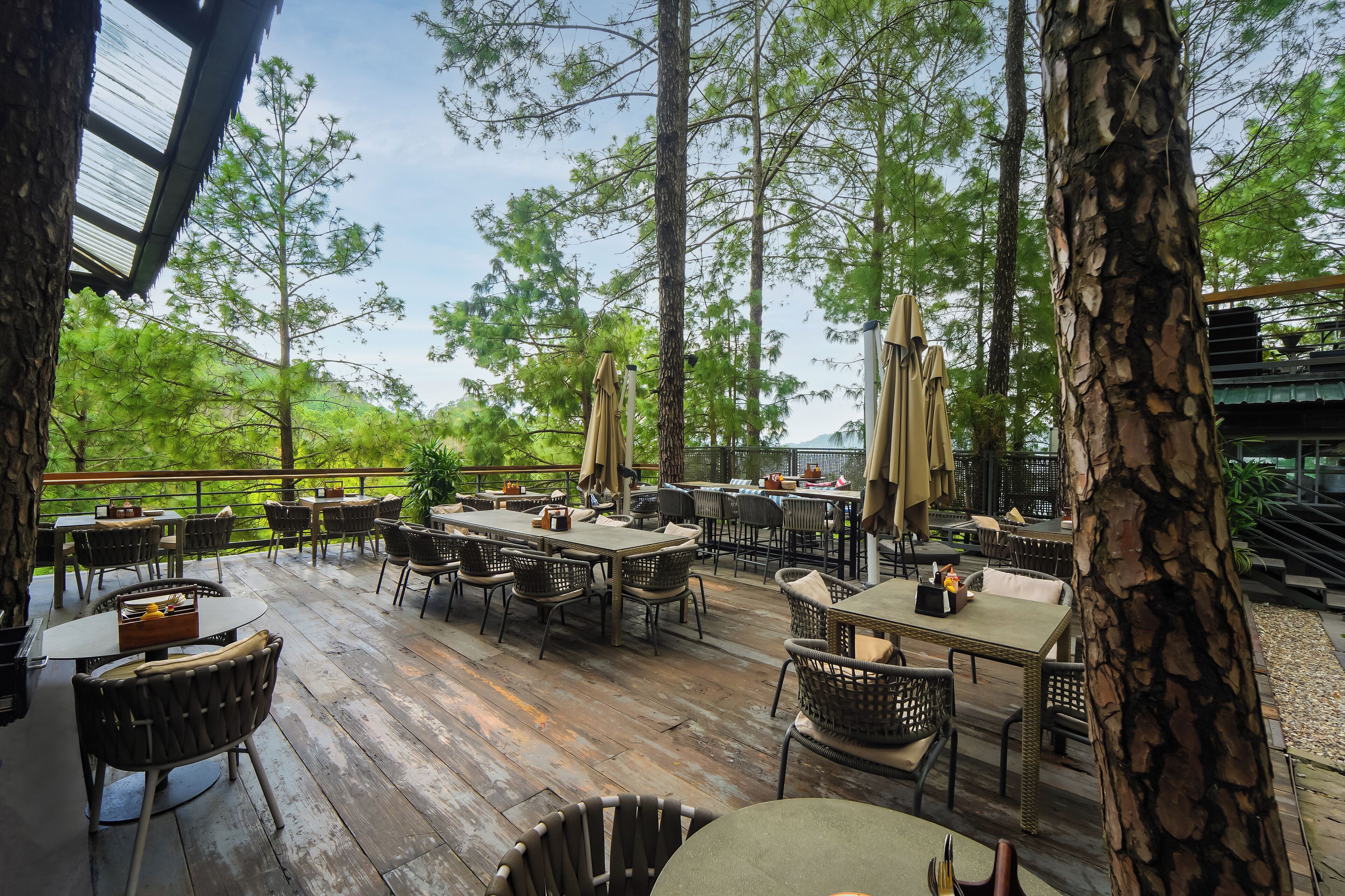 Een terras buiten met houten vloer, tafels, stoelen en parasols.