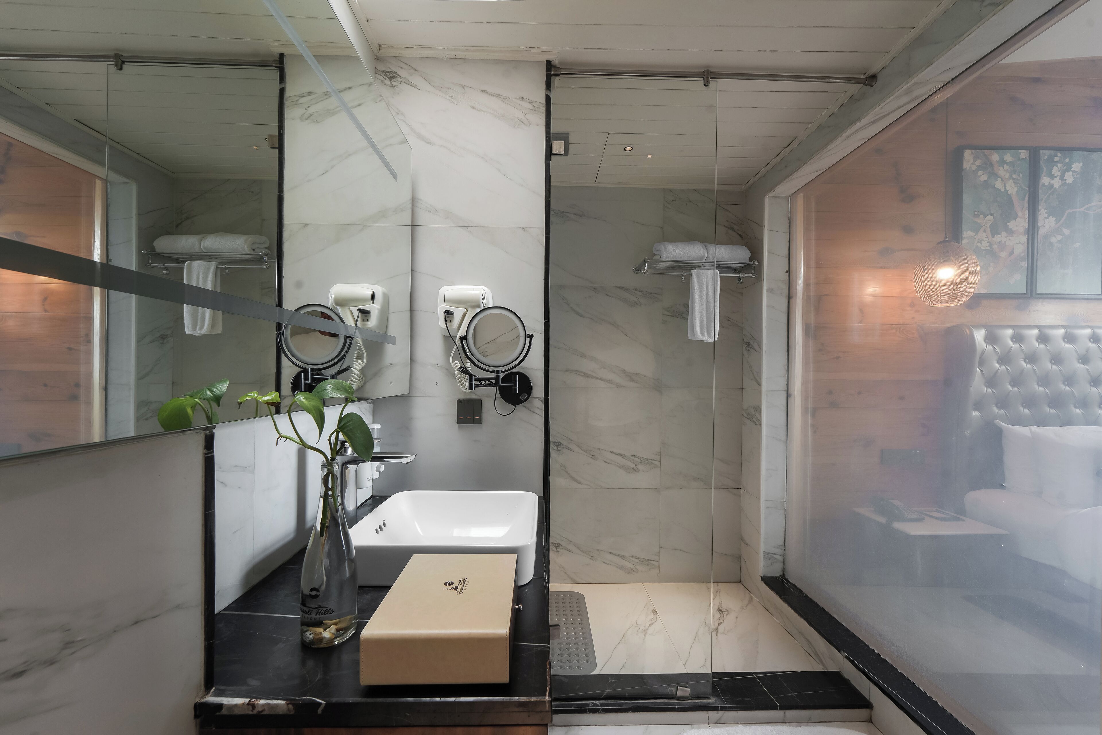 A modern bathroom with a marble sink, a large mirror, a towel rack, and a shower area.