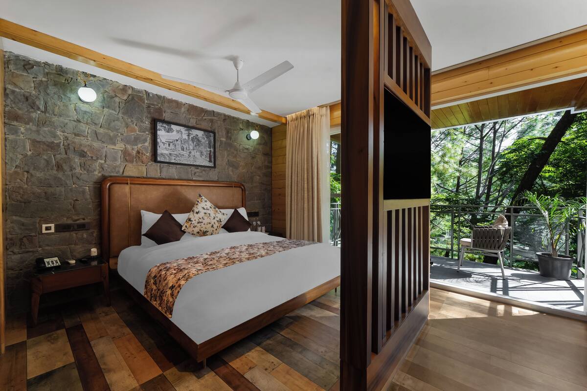Quarto com parede de pedra, cama de madeira, mesa de cabeceira e vista para o verde lá fora.