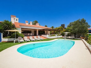 Uma piscina com espreguiçadeiras, um alpendre coberto e um edifício com telhado em azulejo.