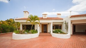 A two-story house with a red-tiled roof, white walls, and a brick patio.