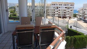 Un balcon avec deux chaises et une table, donnant sur un quartier résidentiel avec des immeubles et un ciel dégagé.