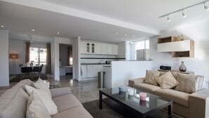 Un salon moderne avec un canapé et une table basse, un coin cuisine avec des meubles blancs et un coin repas avec une table et des chaises.