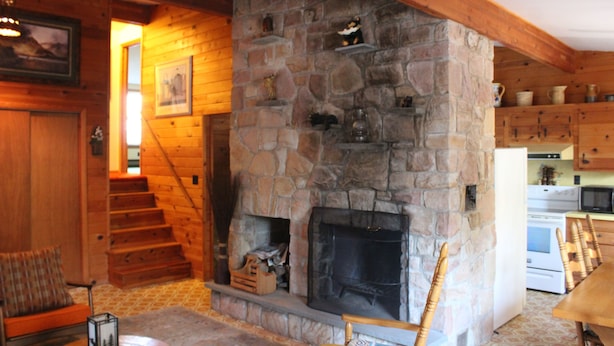 Un interior acogedor de cabaña con chimenea de piedra, escalera de madera y zona de comedor.