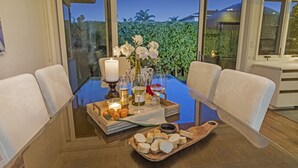 Una mesa de comedor con una vela, copas de vino, un florero con flores y una tabla de madera con lonchas de queso.