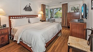 Un dormitorio bien iluminado con una cama grande, piso de madera, un escritorio con silla, un aparador y un televisor en la pared.