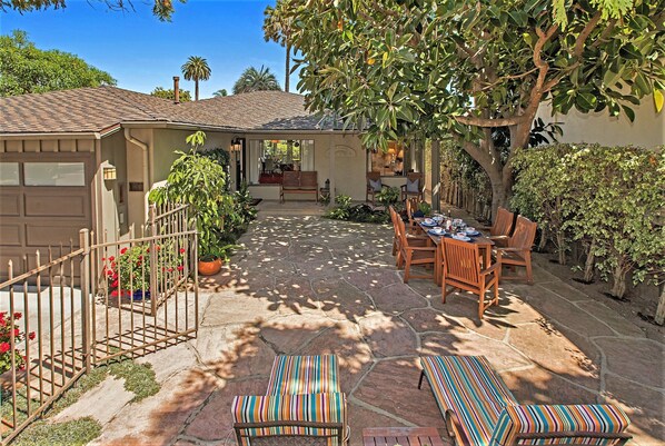 A patio with stone flooring, a wooden table with chairs, and striped cushions.