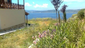 Ein Küstenanwesen mit einem Holzbalkon mit Meerblick, umgeben von üppiger Vegetation und blühenden Pflanzen.