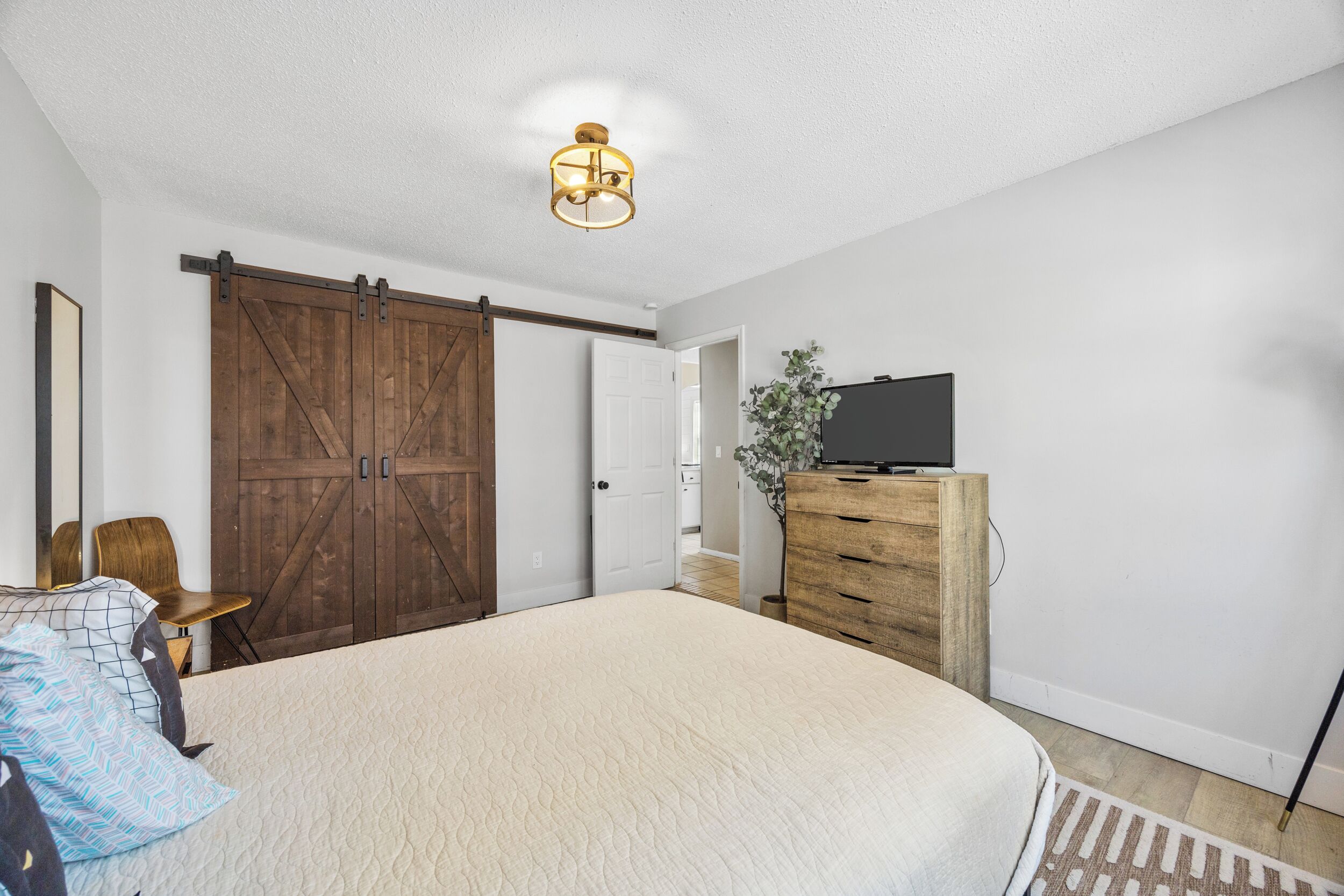 A bedroom with a large bed, a wooden wardrobe, a television on a dresser, and a sliding barn door.