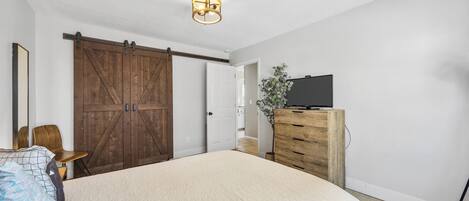 A bedroom with a large bed, a wooden wardrobe, a television on a dresser, and a sliding barn door.