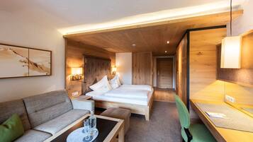 A hotel room with a bed, a sofa, a small table with glasses, and a desk with a chair.