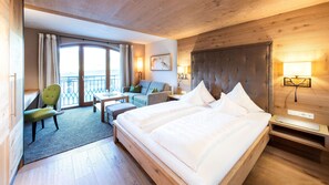 Habitación de hotel con una cama grande, un sofá, una silla, un escritorio y un balcón con cortinas.