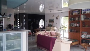 Un salon comprenant un canapé, une table basse, une bibliothèque et un coin cuisine avec un réfrigérateur et un évier.