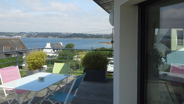Un balcon avec une table et des chaises, donnant sur une étendue d’eau et une côte lointaine.