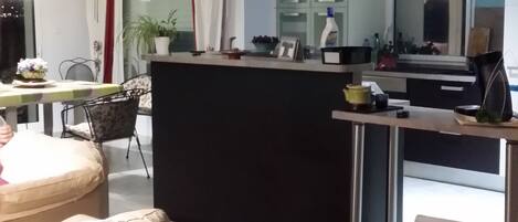 Una sala de estar moderna con un sofá negro central, una mesa de centro con camino de mesa a cuadros y una zona de comedor con mesa y sillas.