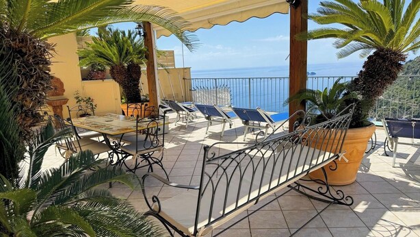 Eine Terrasse mit Tisch und Stühlen, Blumentöpfen und Blick auf das Meer.