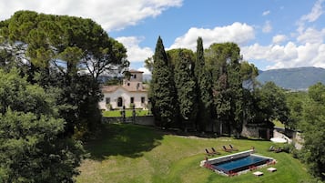 Une villa avec piscine, entourée d’une végétation luxuriante et de grands arbres.