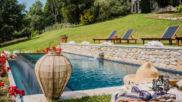 Een zwembad met ligbedden, een stenen muur en een grote decoratieve vaas.