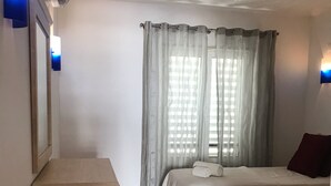 A hotel room with two beds, a wooden desk, a wicker basket, and a window with sheer curtains. - Marina View apartment with personal WiFi & UK TV (Unknown)