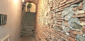 A staircase with a brick wall on one side and a plain wall on the other, leading to a room with a plant.