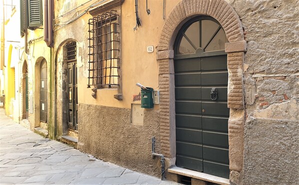 A narrow street with historic buildings, a mailbox, and a door with a metal gate.