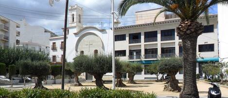 A public square with palm trees, a church, and a building with balconies.