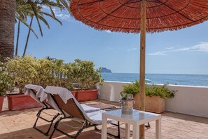 A balcony with a red umbrella, lounge chairs, and potted plants overlooking the sea. - Beach Front Apartment ‘Oden 6’ in Altea (max. 2 persons) (Altea)