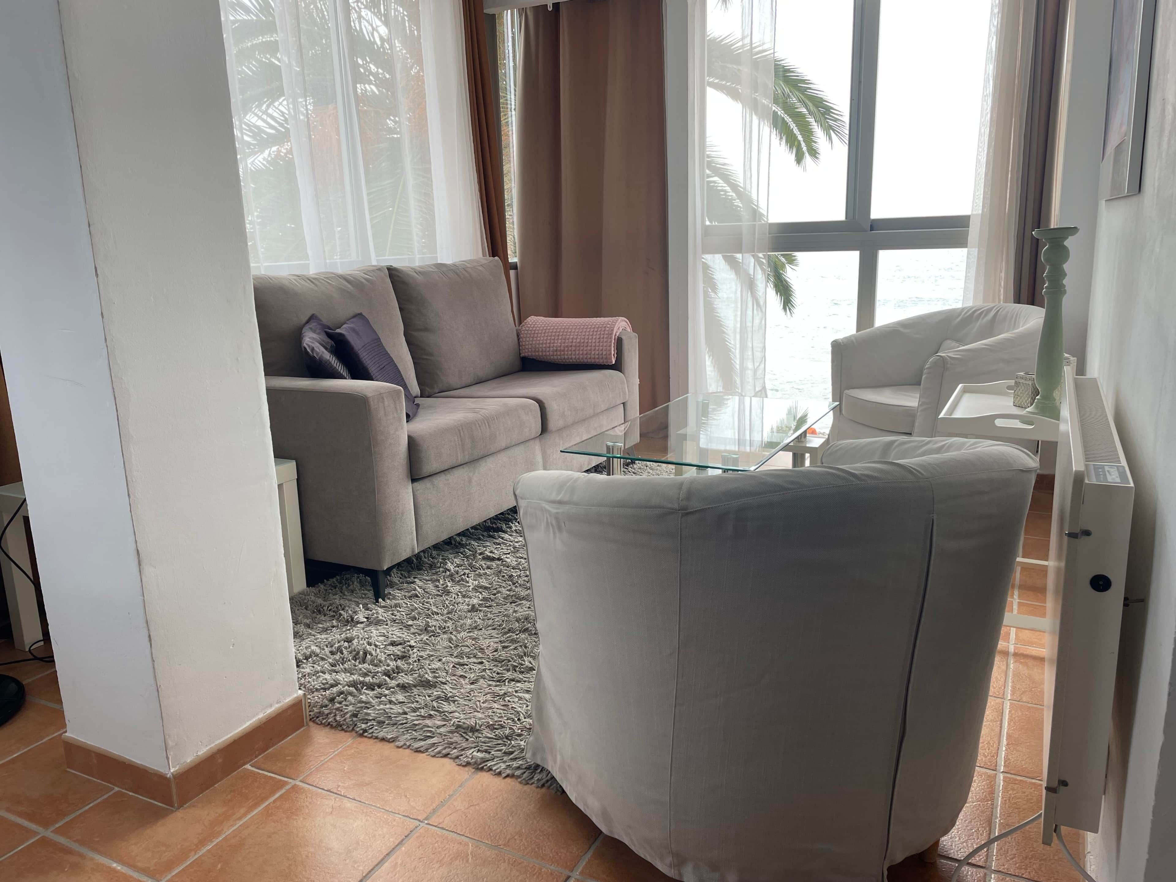 Una sala de estar con un sofá, una mesa de centro de vidrio y un sillón blanco.