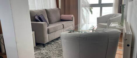 Una sala de estar con un sofá, una mesa de centro de vidrio y un sillón blanco.