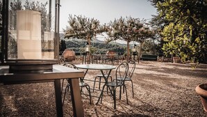 Une terrasse extérieure avec des tables et des chaises, entourée d’arbres et offrant une vue sur les collines.