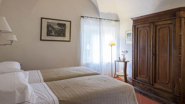 A bedroom with two beds, a wooden wardrobe, a framed picture on the wall, and a small table with a lamp. - Exclusive Villa 18th century, with pool. Fine winery in Chianti central Tuscany (Montevarchi Area)