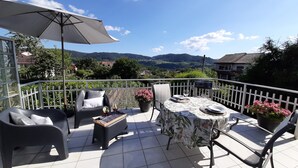 Une terrasse avec une table dressée pour deux personnes, un canapé et une chaise, offrant une vue sur la campagne.
