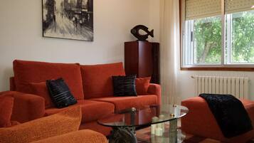 A living room with a red sofa, a glass coffee table, and a black sculpture on a wooden cabinet.