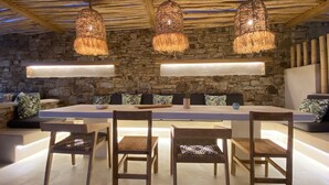 A dining area with a stone wall, wooden ceiling beams, and woven light fixtures.