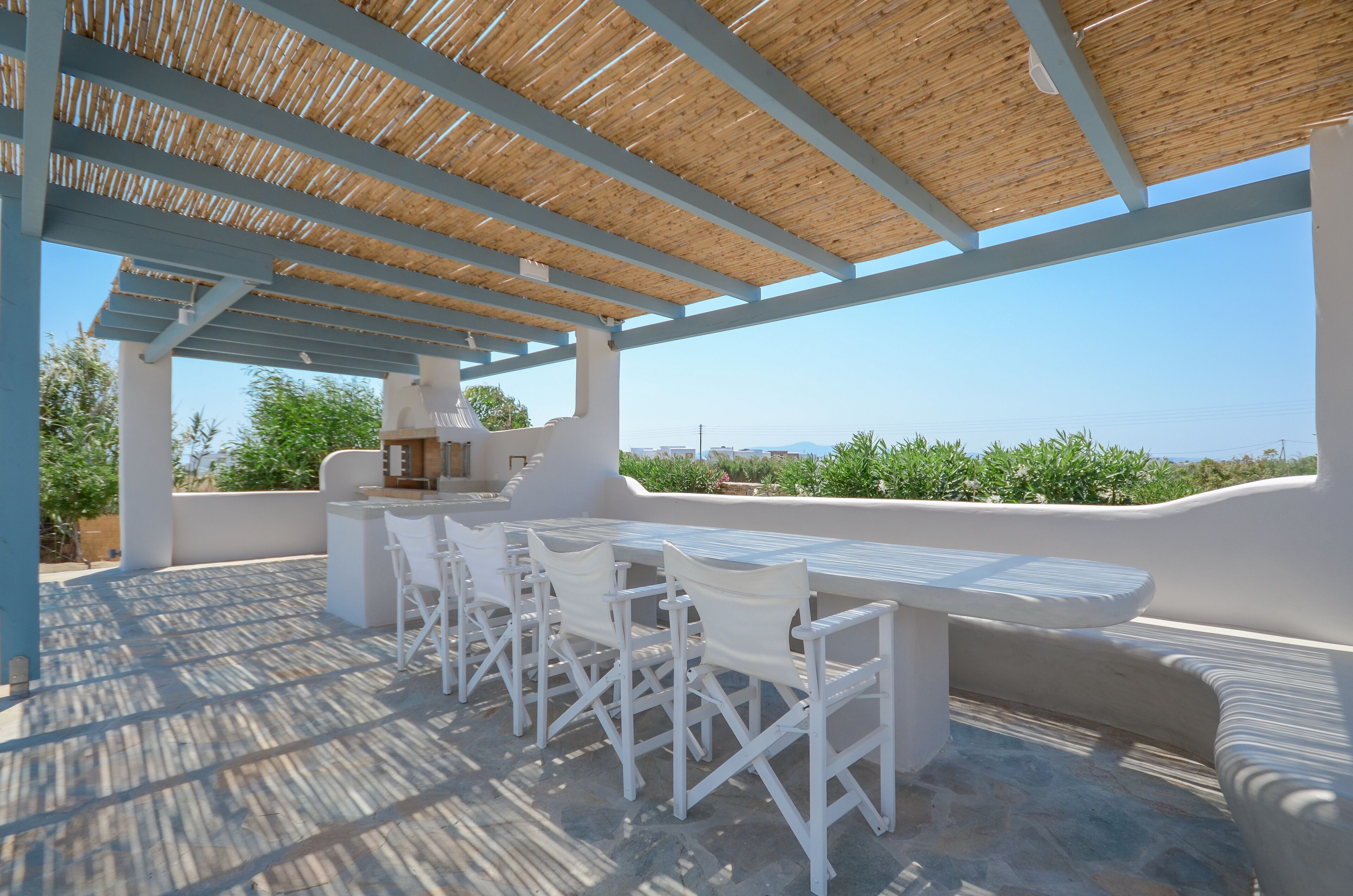 Un patio al aire libre con una pérgola de madera, muebles blancos y vistas al paisaje.