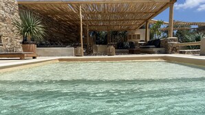 A swimming pool with a stone wall and wooden pergola.