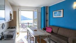 Un espacio habitable compacto con cocina, comedor y sofá. Se ve un balcón con vistas a las montañas a través de una puerta abierta.