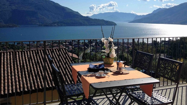 Una terraza con una mesa y sillas que da a un lago, con montañas al fondo.