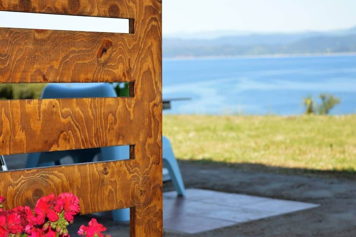 Una estructura de madera con listones horizontales y una superficie reflectante, con vistas a un cuerpo de agua y vegetación.
