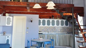 Una habitación amplia con techo alto, un comedor con sillas azules, una cocina con salpicadero de azulejos y una escalera con barandilla de hierro forjado.