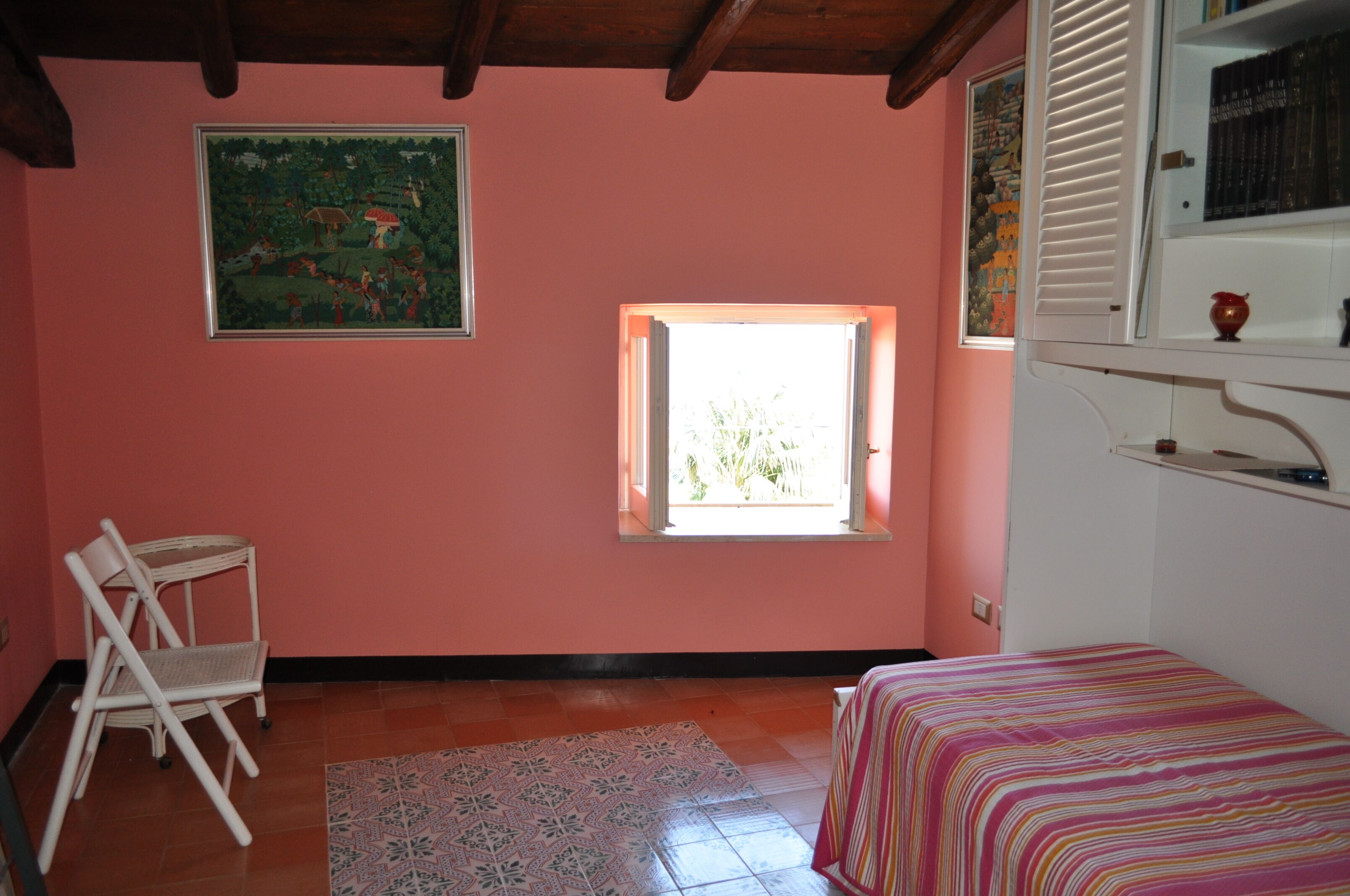 Une pièce avec un lit, une chaise, une fenêtre et un tableau au mur.