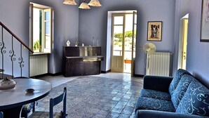 Una habitación con mesa de comedor, sofá, suelo estampado y vistas a través de una puerta abierta.