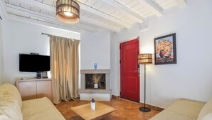 A living room with a TV, sofa, coffee table, fireplace, and a red door. - Superior Suite with Sea View / Varos Village Boutique Hotel (Lemnos)