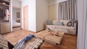 A modern living room with a sofa, coffee table, and a dining area. There is a closet with hanging clothes and a bed in the background. - Superior Suite with Sea View / Varos Village Boutique Hotel (Lemnos)