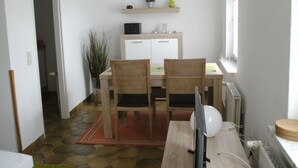 A compact kitchen with a dining table, two chairs, a small refrigerator, and a window.