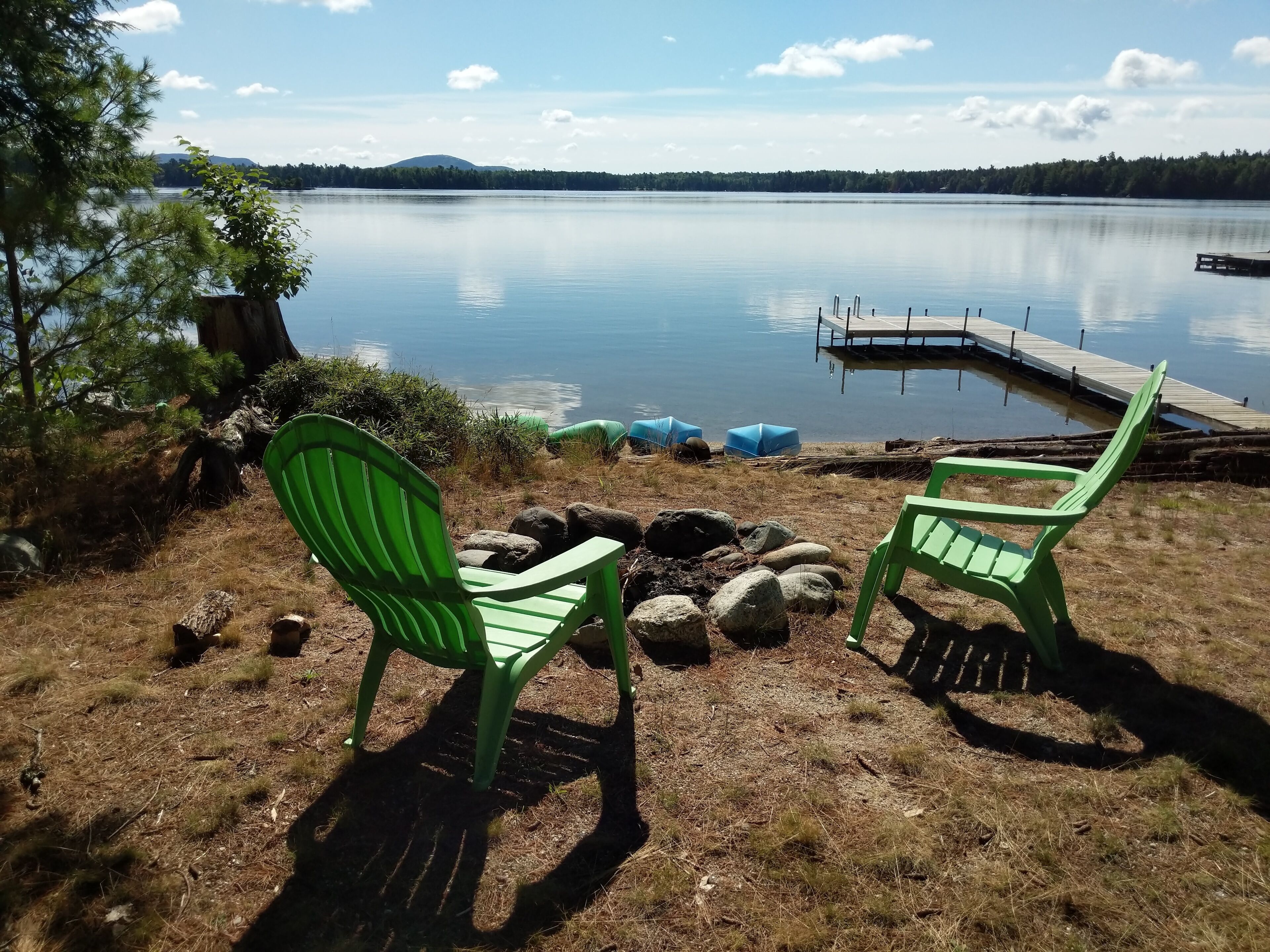 Kaksi vihreää Adirondack-tyylistä tuolia, jotka on asetettu vastakkain rauhallisen järven ääreen. Järvellä on laituri ja sen rannalla kasvaa metsää.